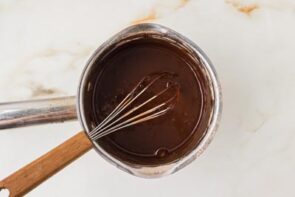 Chocolate ganache being whisked in a saucepan until smooth and glossy.