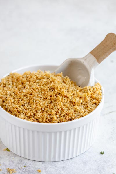 A large white bowl filled with keto breadcrumbs with a scoop inside.