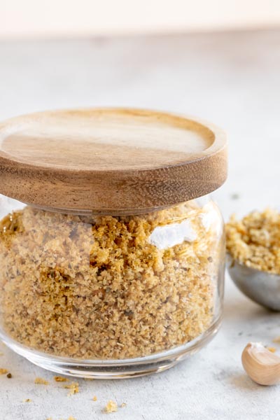 Bread crumbs stored in a small glass jar with a bamboo lid. A clove of garlic sits nearby.