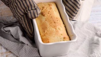 holding a hot loaf of bread in a pan with oven mits