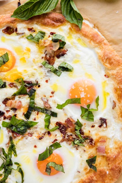 whole eggs cooked into a pizza with bacon and sliced basil