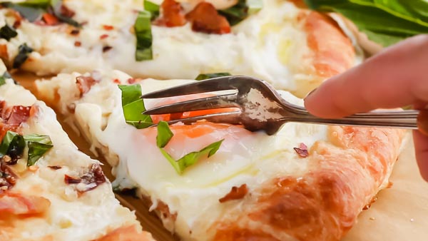 cutting into an egg yolk onto of breakfast pizza