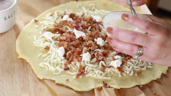 placing dollops of garlic white sauce on a keto breakfast pizza