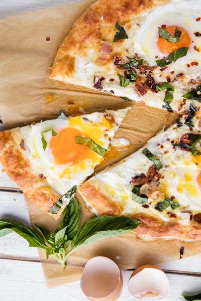 a runny egg sits on top of a slice of pizza with basil leaves nearby