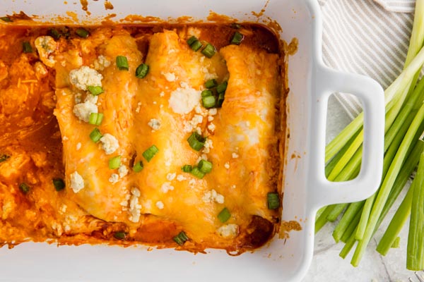 chicken enchiladas in a casserole dish with two missing