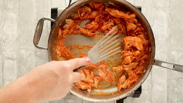 stirring buffalo sauce into a skillet of shredded chicken