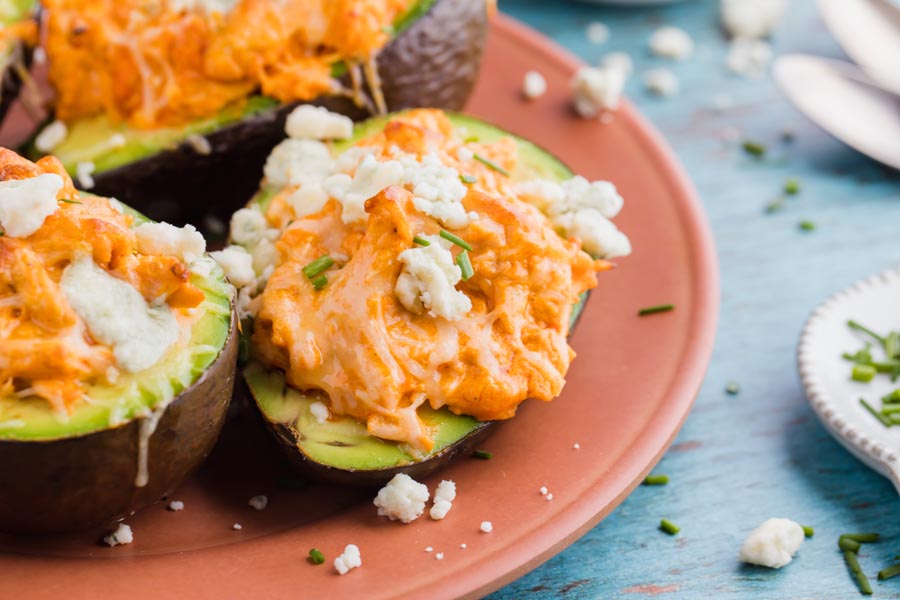 creamy buffalo chicken sits inside a green avocado and topped with crumbled blue cheese