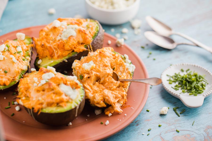a spoon is digging into a buffalo chicken stuffed avocado on a red plate