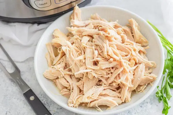 a bunch of shredded chicken in a white bowl next to an instant pot