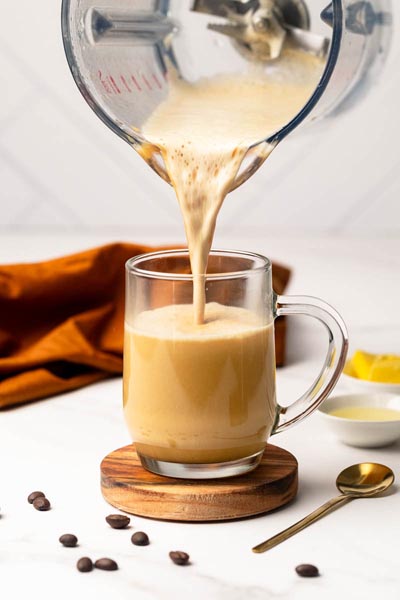 Freshly blended keto bulletproof coffee being poured from a blender into a clear glass mug.