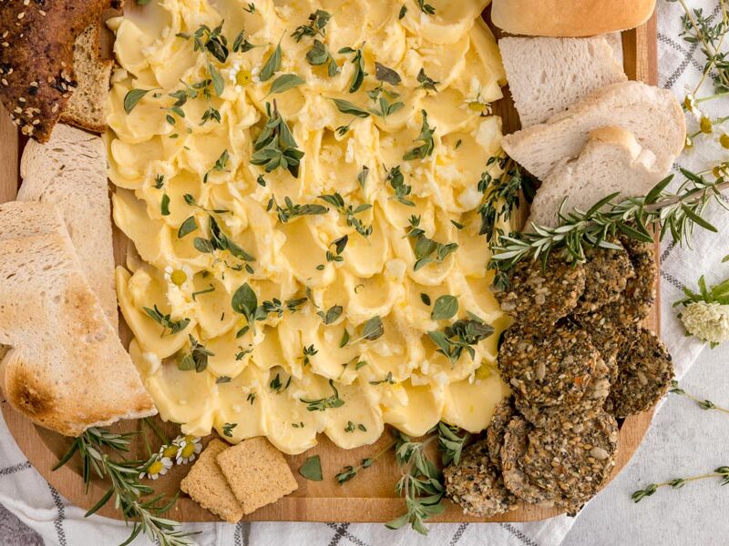 yellow butter spread on a platter and topped with lemon zest, herbs and garlic with crackers around