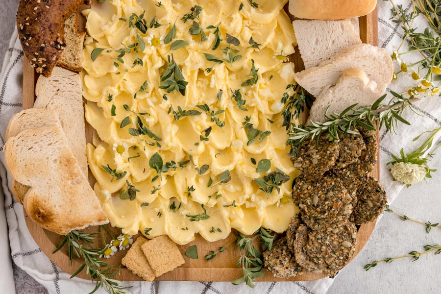 yellow butter spread on a platter and topped with lemon zest, herbs and garlic with crackers around