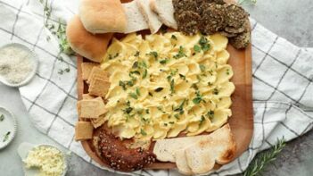 a butter board platter surrounded by rolls, crackers and slices of keto bread