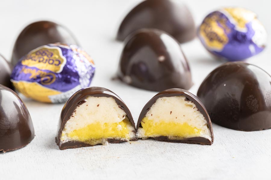a cadbury eggs sliced in half with other chocolate eggs and foil wrapped eggs behind it