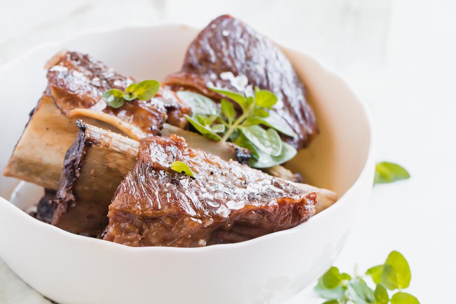 juicy fall off the bone short ribs in a white bowl with thyme leaves on top