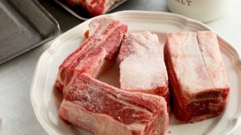 beef short ribs on a white plate sprinkled with salt