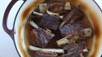 cooked short ribs in a dutch oven with the meat pulled back from the bone