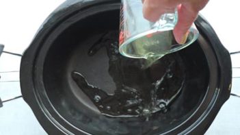 pouring apple cider vinegar to the black liner of the slow cooker