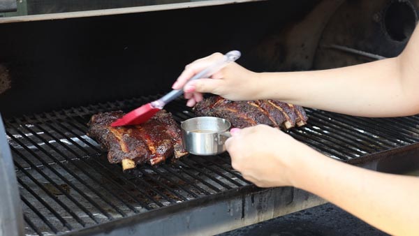 basting beef back ribs with a beef broth and vinegar mixture using a red rubber brush