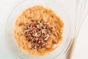 a bowl of carrot cake batter with nuts on top and a wire whisk near by