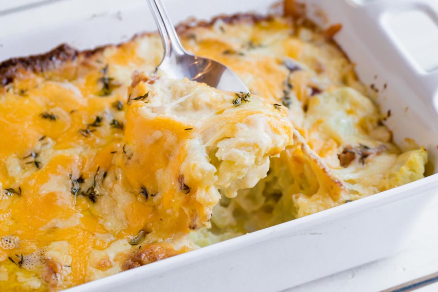scooping out some cheesy cauliflower gratin from a serving dish