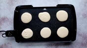 an electric griddle with six pancakes cooking on the first side