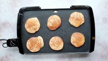six pancakes flipped and cooking on a griddle