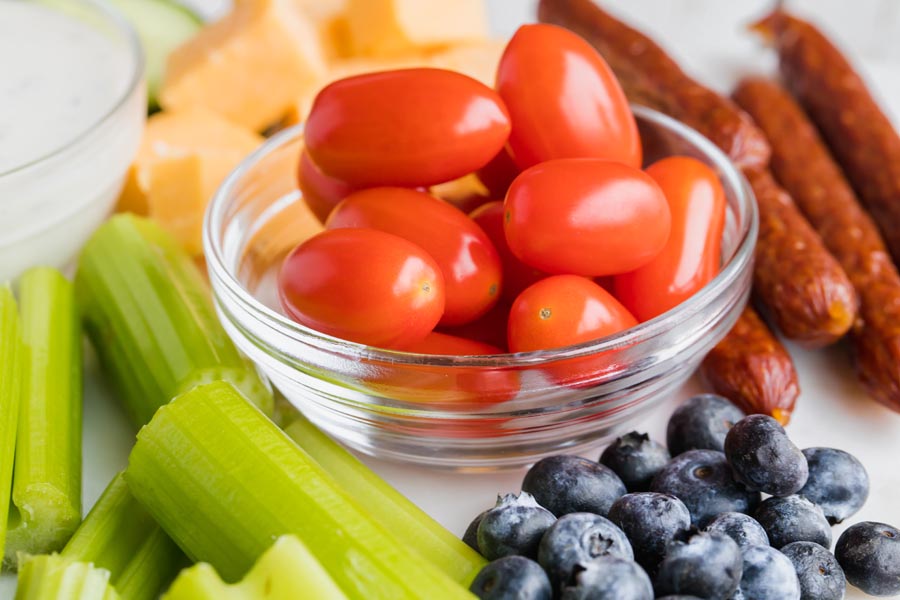 bright red cherry tomatoes in a bowl next to celery, beef sticks and blueberries