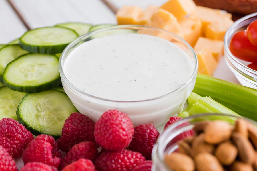 ranch dressing in a small bowl surrounded by fruits and vegetables