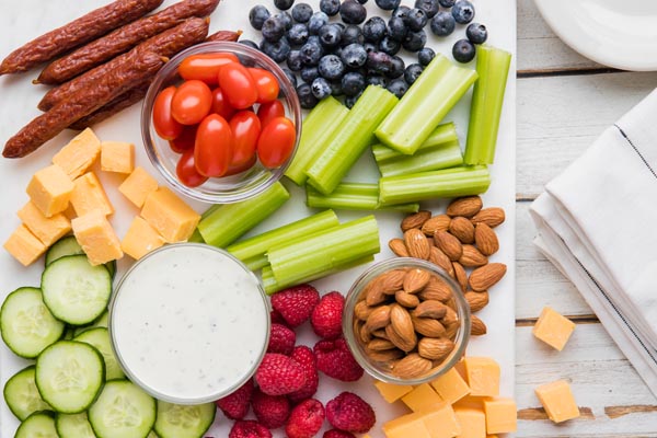 cheeses, veggies and fruits on a white board next to napkins