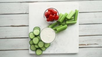 cucumber, celery, tomatoes and ranch dressing scattered on a marble board