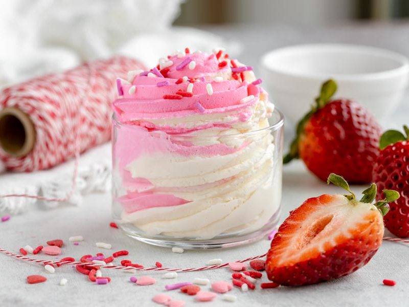 Pink and white cheesecake fluff in a glass bowl with sprinkles and fresh strawberries.