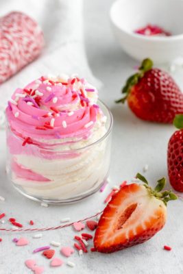 a half strawberry slice sits in front of a small bowl of fluffy cheesecake filling topped with heart sprinkles