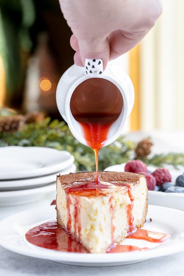 pouring a thick red syrup over a plain cheesecake
