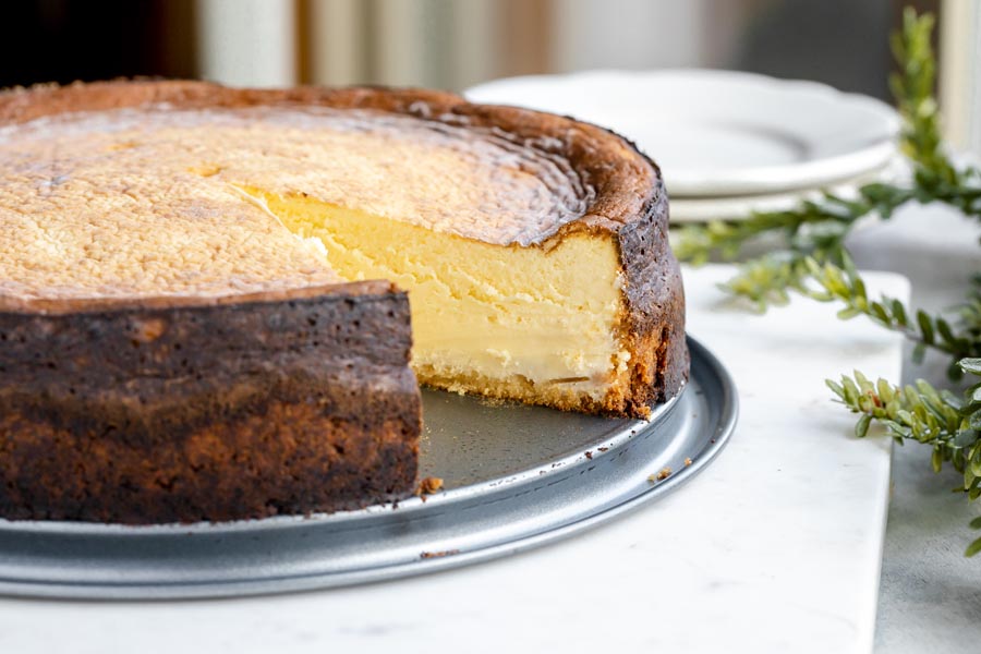 a whole cheesecake with a slice taken out with plates in the background