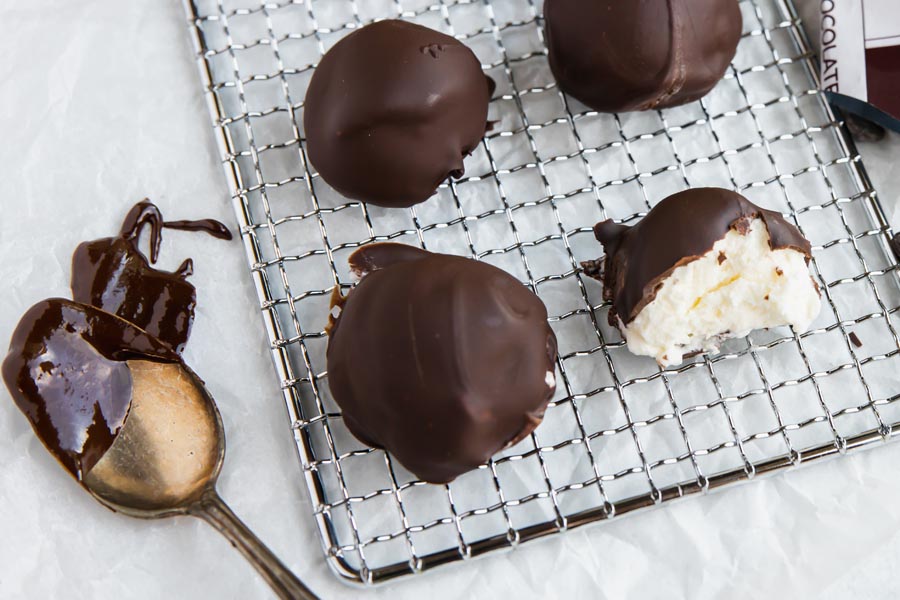 four cheesecake balls on a wire rack with a spoon and melted chocolate next to it