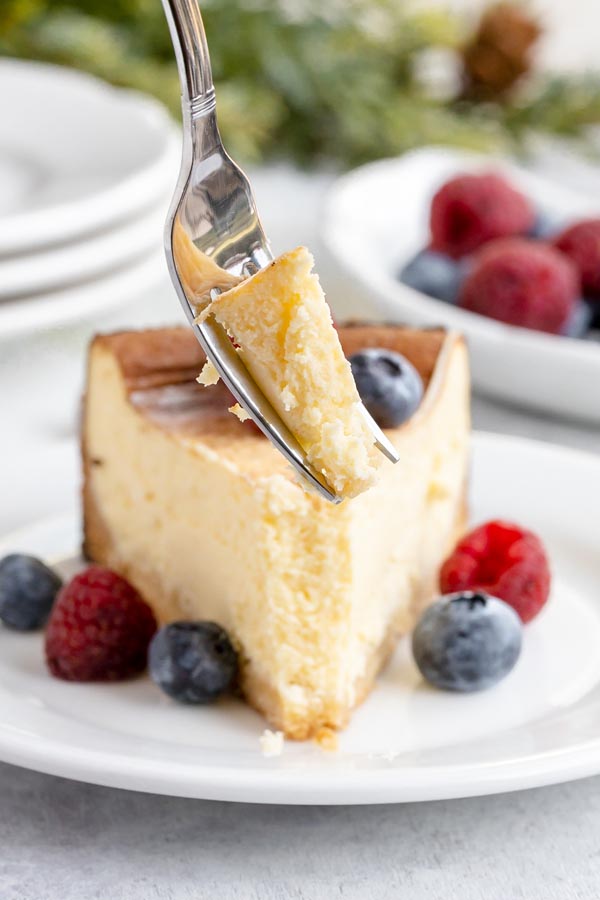a fork holding a bite of cheesecake with a slice in the background covered in berries