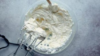 smooth cream cheese in a bowl with a spatula stuck in and electric mixer beaters above