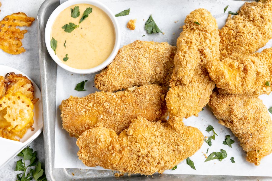 a tray with crispy chicken strips next to a small bowl with chick-fil-a sauce topped with chopped parsley