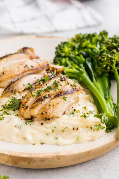 A plate of creamy alfredo topped with grilled chicken and parsley.