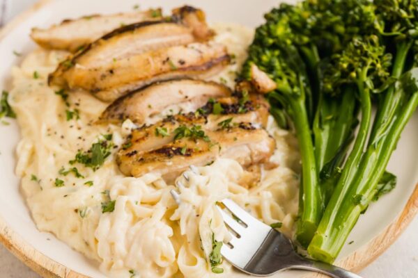 A fork holding fettucine noodles coated with creamy sauce and topped with chicken thighs.