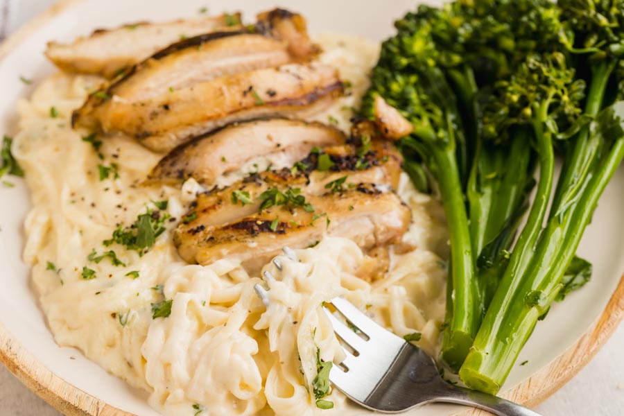 A fork holding fettucine noodles coated with creamy sauce and topped with chicken thighs.