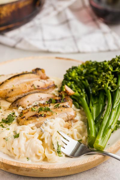 A dinner plate with noodles and grilled chicken. A fork has pasta tangled around it.