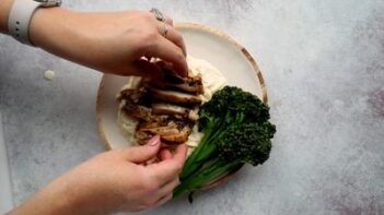 Hands placing cooked chicken on top of alfredo noodles.