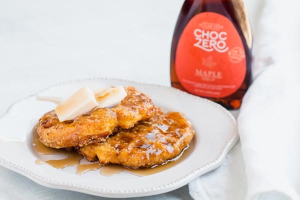 two waffles on a plate covered in syrup with a bottle of syrup next to it