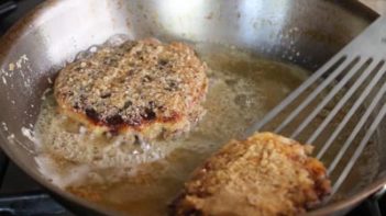 flipping a fried chicken waffle with a spatula that is in a frying pan