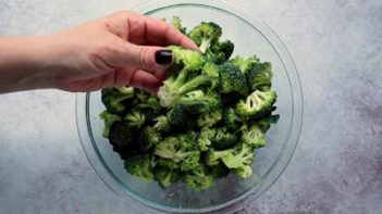 holding a broccoli floret over a bowl of broccoli