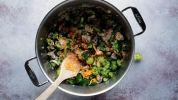 stirring a large pot with chicken, broccoli and cheese with a wooden spoon