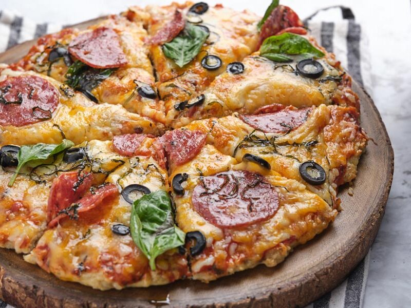 A whole pizza topped with olives, basil, and pepperoni.