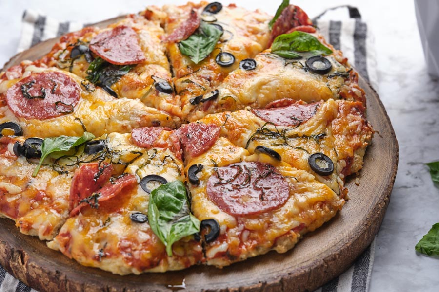 A whole pizza topped with olives, basil, and pepperoni.